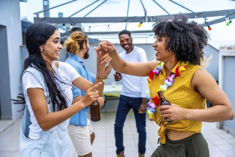 Cheerful young friends are dancing and having fun at a rooftop party, enjoying drinks and each