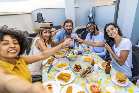 Cheerful multi ethnic friends enjoying rooftop barbecue party, taking selfie and toasting with