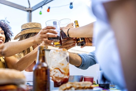 Diverse group of friends enjoying barbecue food and drinks, toasting together on a rooftop under
