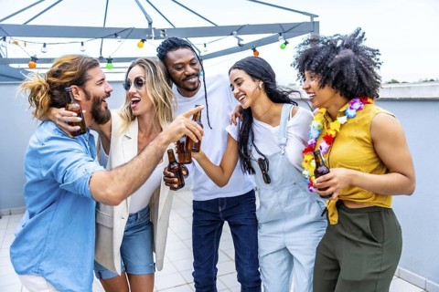 Cheerful multi ethnic friends enjoying drinks at a rooftop party, celebrating their friendship with