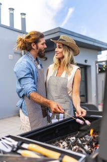 Happy couple enjoying a sunny summer day, grilling marshmallows on a rooftop barbecue, sharing