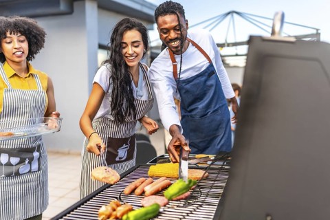 Happy friends enjoying a rooftop barbecue party, grilling delicious food, sipping drinks, and