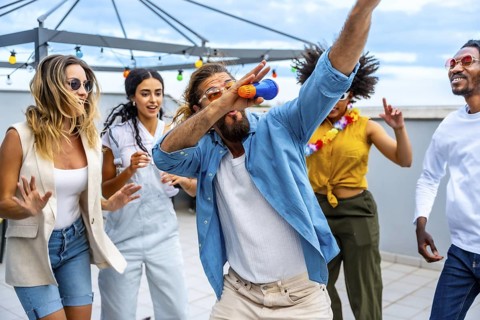 Diverse group of friends celebrating on a vibrant rooftop, singing and dancing joyfully together,