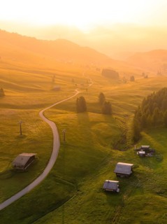 Undulating hills and forests in sunset mood with scattered mountain huts, Alpe di Siusi, Dolomites,