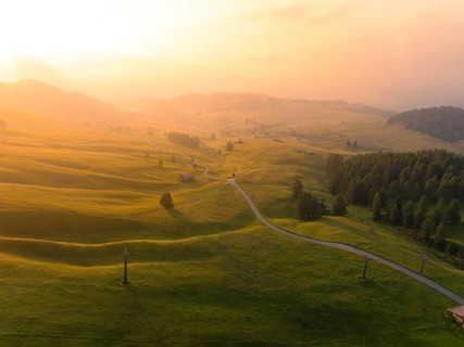 Soft hills and meadows in the golden light of sunset with scattered mountain huts, Alpe di Siusi,
