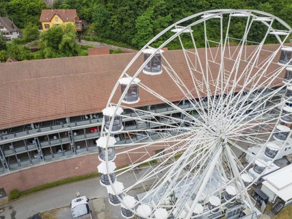 Close-up of the Ferris wheel with detailed view of the cabins and buildings in the background,