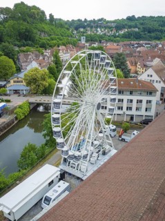 A large Ferris wheel towers over the city centre, surrounded by the river and green landscape,