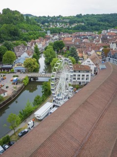 View of a Ferris wheel in an urban area with a river and hilly, green surroundings, construction of