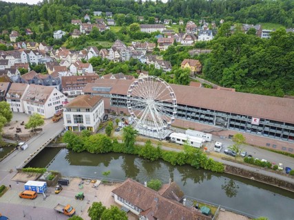 A Ferris wheel next to a river in the centre of a town with a green hilly landscape in the