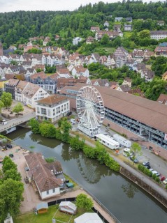 Aerial view of an idyllic village with a Ferris wheel by the river and surrounded by green hills,
