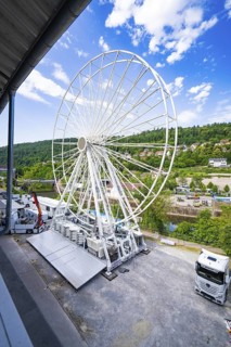 Construction phase of a Ferris wheel next to lorries in a rural setting, Ferris wheel construction