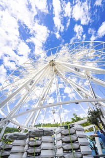 Partially erected Ferris wheel in front of a clear blue sky with cloud formations, Ferris wheel