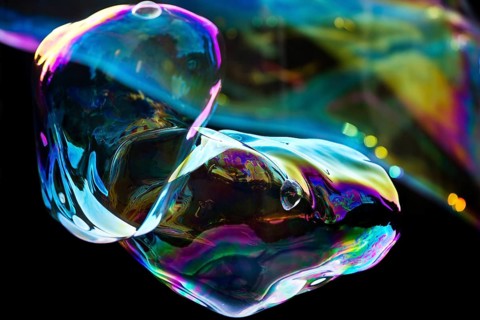 Irregular, iridescent soap bubble in the colours of the rainbow against a black background,