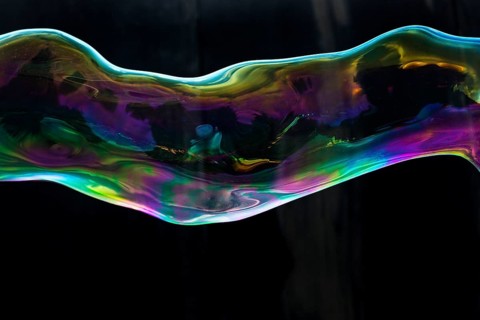 Large, iridescent soap bubble tube in the colours of the rainbow against a black background,