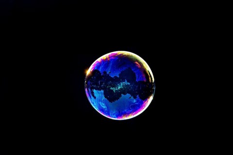 A shimmering and floating soap bubble in the colours of the rainbow against a black background,
