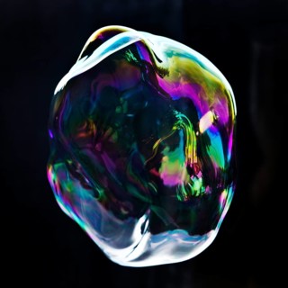 A large iridescent and floating soap bubble in the colours of the rainbow against a black