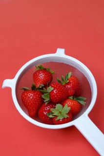 Strawberries in a colander on a red background, Fragaria