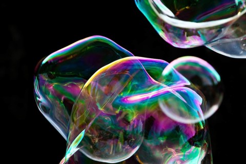 Large, irregular, iridescent soap bubbles in the colours of the rainbow against a black background,