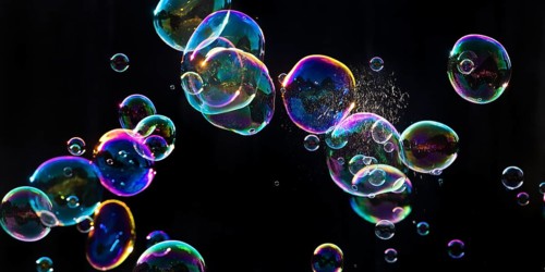 Iridescent soap bubbles with a just burst bubble in front of a black background, Recklinghausen,