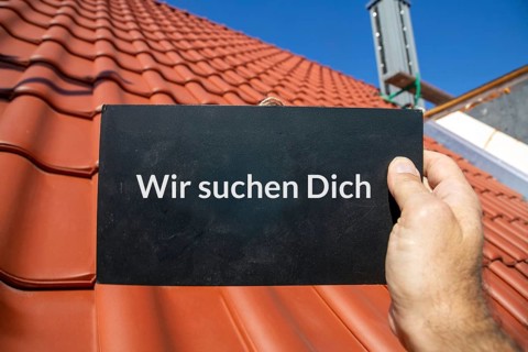 Employee search roofer: Man holding a sign (with added text) WE ARE LOOKING FOR YOU in front of a