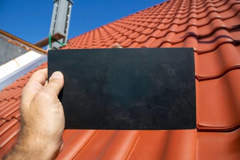 Man holding a sign with space for text in front of a recently tiled roof