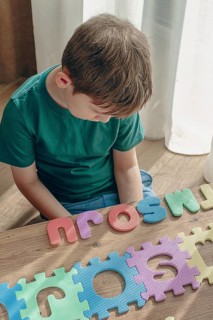 Boy with autism, expresses frustration, playing with puzzle pieces, on a wooden table, natural