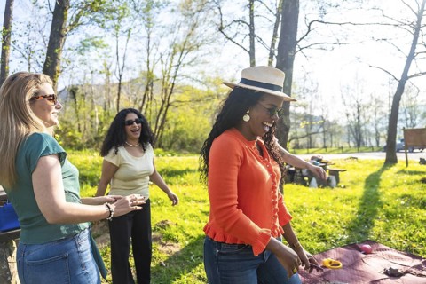 Three female friends enjoying a picnic in a park, playing and laughing together on a beautiful