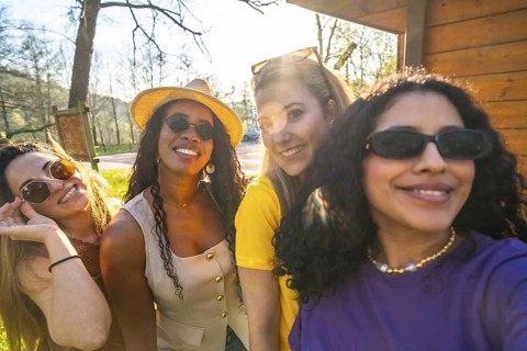 Four cheerful women enjoying a sunny day in the park, smiling and capturing memories together while
