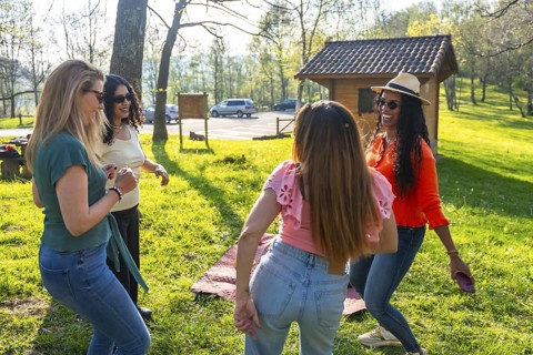 Four beautiful multi ethnic women dancing and having fun at a picnic in a park during a sunny day