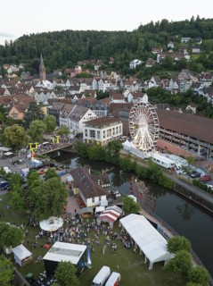 City festival with Ferris wheel and tents by the river on wooded hills, 950 years of Calw, Germany