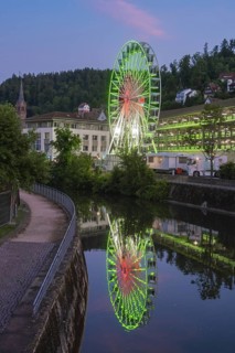 Close-up of a green illuminated Ferris wheel in front of an evening sky with pink clouds, 950 years
