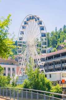 A white Ferris wheel in daylight against a backdrop of buildings and wooded hills, 950 years of