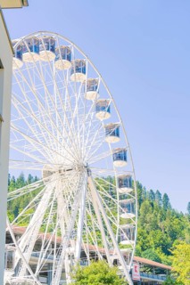 A Ferris wheel with numerous cabins stands close to a building, against a green background and blue