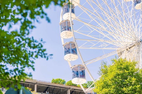 Close-up of a Ferris wheel with cabins, visible between green trees and a blue sky, 950 years Calw,