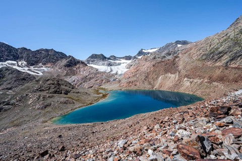 Mountaineer on hiking trail, view of blue glacial lake in rocky mountain landscape, behind
