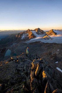 Mountaineer in front of picturesque high mountain landscape at sunrise with alpenglow, glacier and
