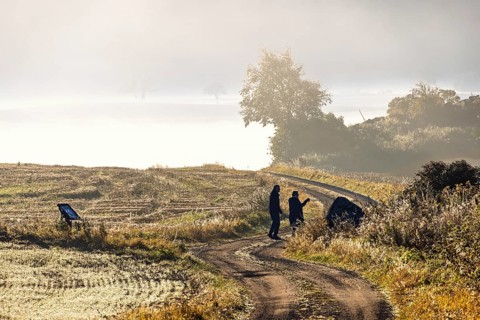 Couple standing on a winding gravel road in a rolling agricultural landscape with low morning mist