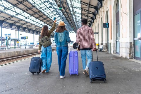 Three young tourists are walking inside a train station pulling their trolley bags and a