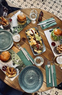 Top view of a wooden restaurant table with nachos, burgers, french fries, and beer, suggesting a
