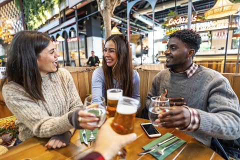 Group of cheerful multi ethnic friends toasting with beer and water at brewery pub restaurant,