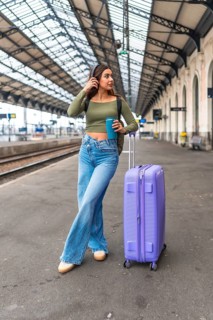 Stylish tourist listening to music while waiting for her train at a station platform, enjoying a