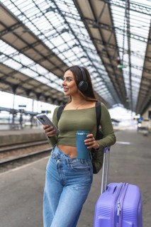 Tourist is waiting for train departure at railway station listening to music on headphones and