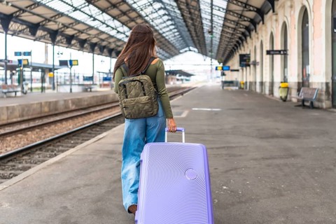 Tourist walking on railway platform pulling trolley suitcase and wearing backpack, traveling by