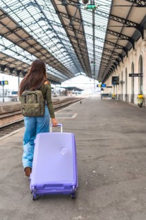 Tourist walking along a train platform, pulling a trolley suitcase while embarking on an exciting