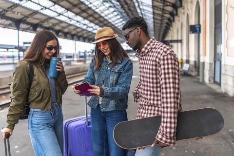 Group of friends looking at passport and travel documents on railway platform, ready for summer
