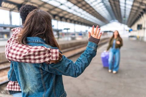Couple waving goodbye to their friend at the train station, sharing a heartfelt moment filled with