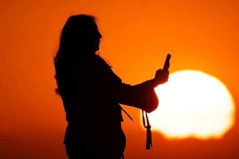 People photographing the sun setting on the horizon with their smartphones from the summit of the