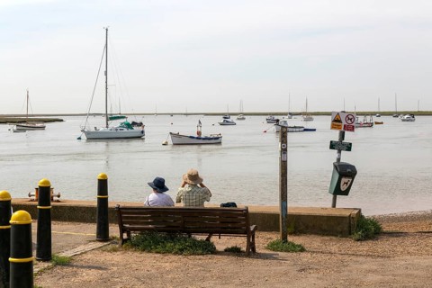 People looking out from quayside at boats moored in harbour, River Ore, Orford, Suffolk, England,