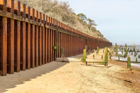 Steel sheet piling sea wall old broken wooden groynes coastal defences, Bawdsey, Suffolk, England,