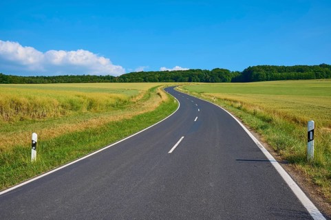 Rural road winds through green fields under a blue sky with white clouds, summer, Marktheidenfeld,